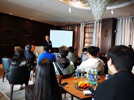 A group of people sitting at a table watching a presentation Description automatically generated with low confidence